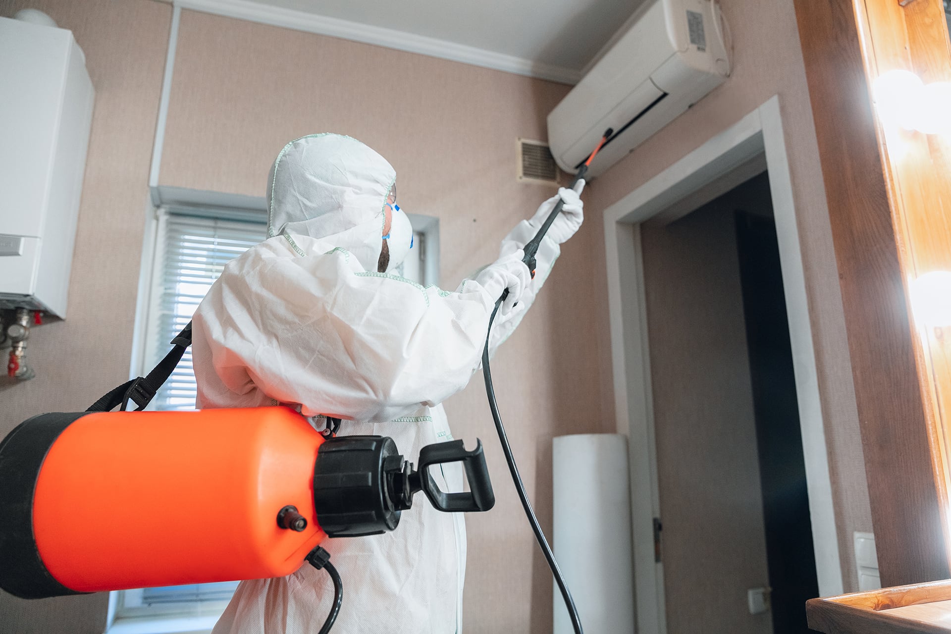 addetto alla sanificazione degli ambienti che utilizza una lancia di pulizia per spruzzare il liquido disinfettante verso uno split di un condizionatore di assitecnica srl